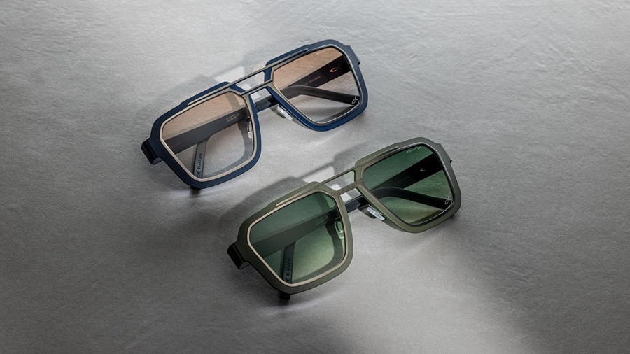 Two pairs of Blackfin One Sun Iron Harbor sunglasses laid flat on a grey surface — one in navy blue with amber gradient lenses, one in olive green with dark green lenses