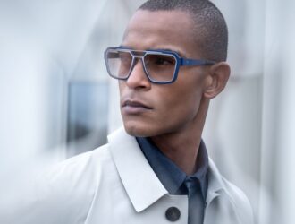 Man wearing Blackfin One Sun Iron Harbor sunglasses in bold blue square titanium frames with a shape-within-a-shape design, styled with a light grey trench coat