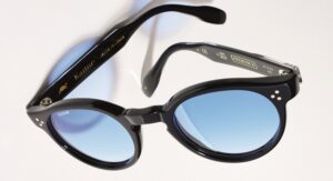 Lunettes de soleil Kador Premium 99 en acétate noir brillant à monture ronde et verres à dégradé bleu clair, posées ouvertes vues de dessus, avec la mention « Fatto in Italia » visible sur la branche.