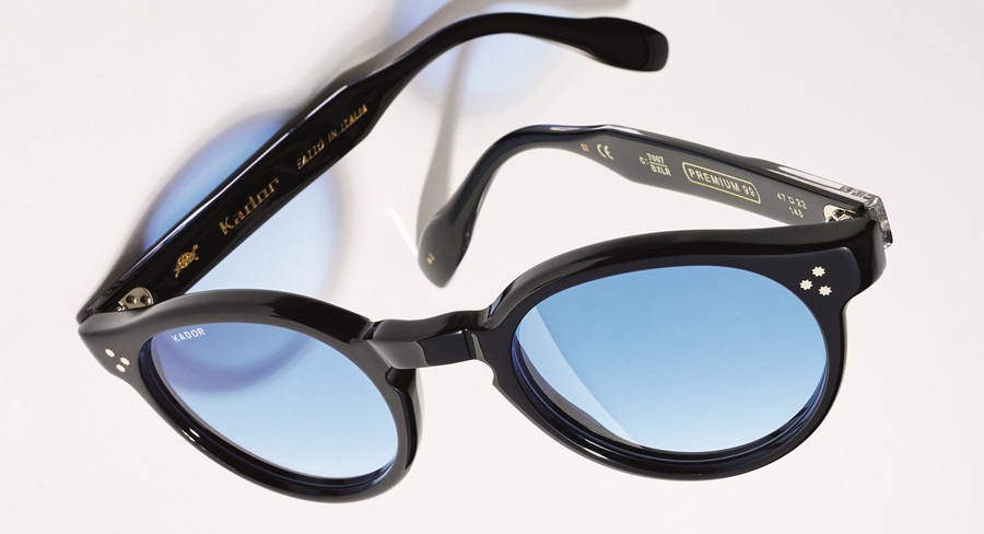Lunettes de soleil Kador Premium 99 en acétate noir brillant à monture ronde et verres à dégradé bleu clair, posées ouvertes vues de dessus, avec la mention « Fatto in Italia » visible sur la branche.