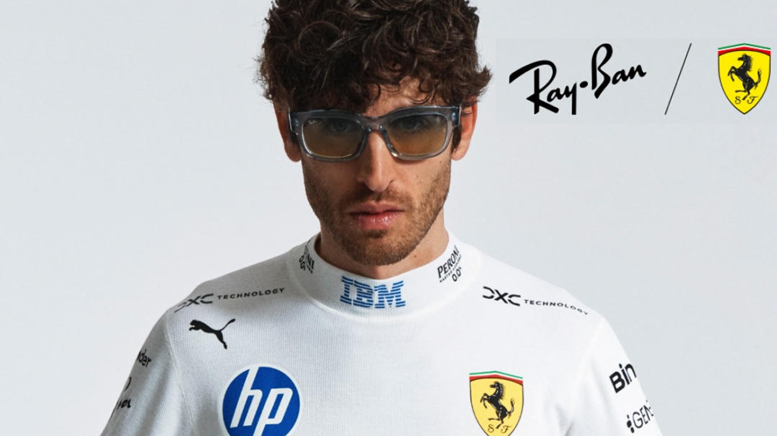 Male model wearing Ray-Ban x Scuderia Ferrari sunglasses in transparent blue frames, dressed in a white Scuderia Ferrari HP race suit, holding a red racing jacket, against a light grey background.