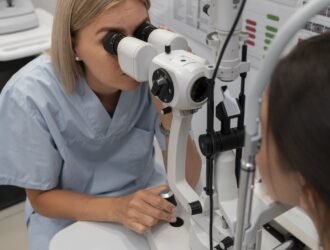 A healthcare professional in blue scrubs examines a patient's eye using a slit lamp in a clinical setting.
