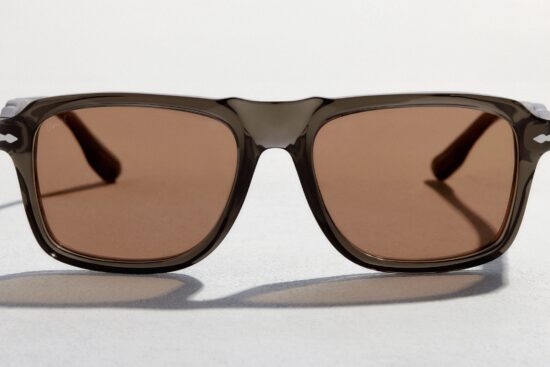Front-facing view of Persol sunglasses featuring a smoke-grey transparent frame and warm brown lenses