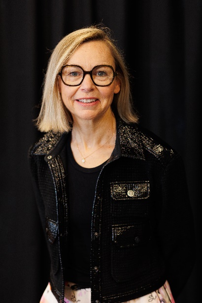 Portrait of Amélie Morel, President of SILMO Paris, smiling and wearing large black-framed glasses and a black embroidered jacket
