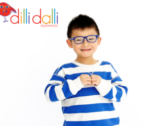 A young boy smiling and wearing blue Dilli Dalli Hero glasses, a blue and white striped sweater, and denim joggers.