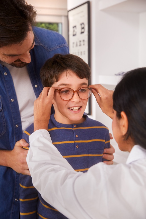 Un opticien ajuste les lunettes d'un jeune garçon dans une clinique ophtalmologique, sous le regard de son père