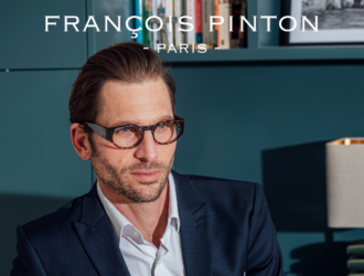 A man wearing tortoiseshell François Pinton glasses and a navy blue suit jacket, sitting in front of a bookshelf.