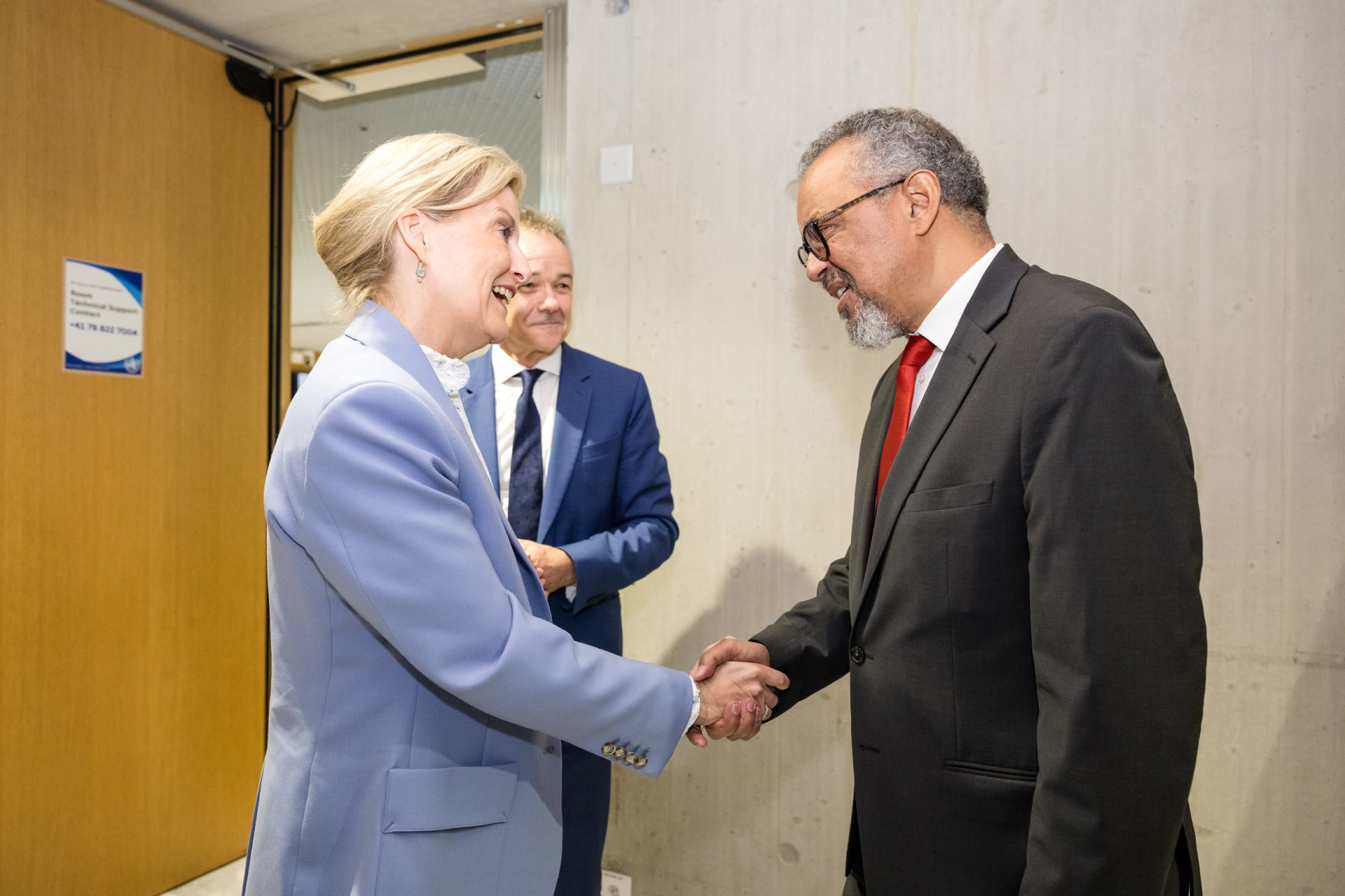 HRH The Duchess of Edinburgh shaking hands and smiling while greeting Dr. Tedros Adhanom Ghebreyesus, Director-General of the World Health Organization. The Duchess is dressed in a light blue professional suit during her visit to the World Health Assembly to advocate for eye health.