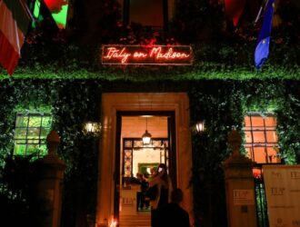 Entrée du lieu de l'événement Italy on Madison de nuit, avec une enseigne néon rouge et une façade couverte de lierre
