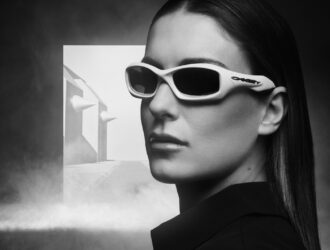A cinematic, black-and-white portrait of athlete Alexia Putellas wearing light-colored Oakley FatCat sunglasses against a misty, architectural background.