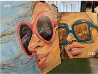 Two large-format oil paintings by artist AnnLo created in collaboration with Transitions®. The 2021 canvas (left) features a close-up portrait of a woman with windswept blonde hair wearing heart-shaped pink sunglasses with dark lenses. The 2022 canvas (right) shows a similar close-up portrait of a woman wearing bold teal square-framed glasses with warm amber-toned reflective lenses, set against a golden ochre background.