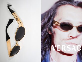 A split-screen Versace Spring Summer 2026 campaign image. On the left, a top-down view of gold metal oval sunglasses with black temples on a white surface. On the right, a grainy, high-contrast portrait of actor Kazuya Tanabe wearing the same gold frames with dark lenses. The white Versace logo is centered at the bottom.