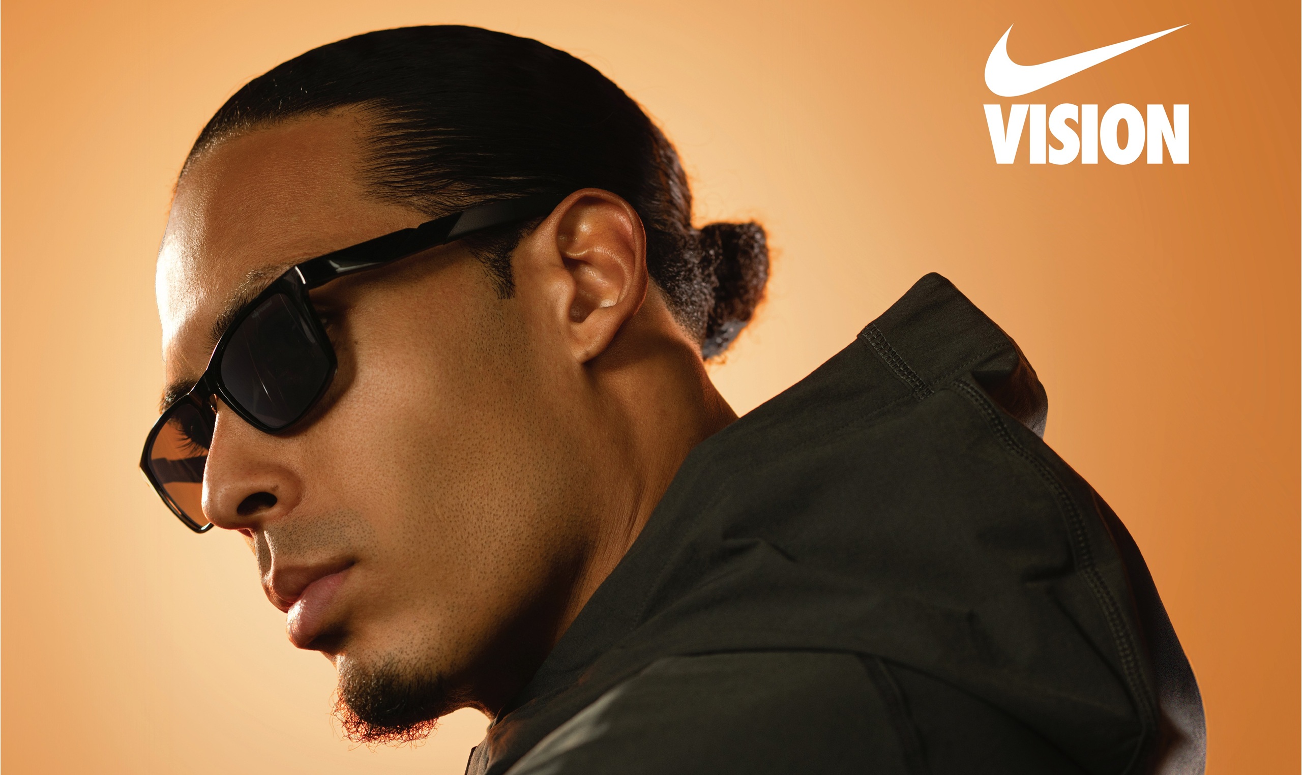 Portrait de profil du footballeur professionnel Virgil van Dijk portant des lunettes de soleil Nike Radeon. Il porte une veste à capuche sombre sur un fond dégradé orange, avec le logo Nike Vision visible en haut à droite.