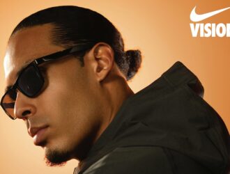 A profile shot of professional footballer Virgil van Dijk looking downward while wearing Nike Radeon sunglasses. He is wearing a dark hooded jacket against a warm, orange-gradient background. The Nike Vision logo is displayed in the top right corner.
