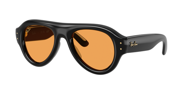 A three-quarter view of the Ray-Ban Aviator Puffer sunglasses (Model 0RB4925). The classic pilot silhouette is reinterpreted with an exaggerated, thick, rounded black frame. It features solid orange-tinted lenses, wide glossy black temples with a gold script Ray-Ban logo, and two small vertical gold pins on each side of the frame front.