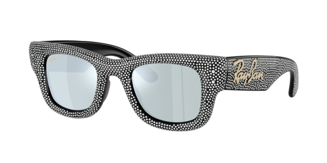 A three-quarter view of the Ray-Ban Wayfarer Puffer sunglasses (Model 0RB4940) designed in collaboration with A$AP Rocky. The entire thick, inflated frame and temples are heavily encrusted with a dense crystal pavé detailing against a black base. It features light silver mirrored lenses and a prominent gold script Ray-Ban logo on the side temple.