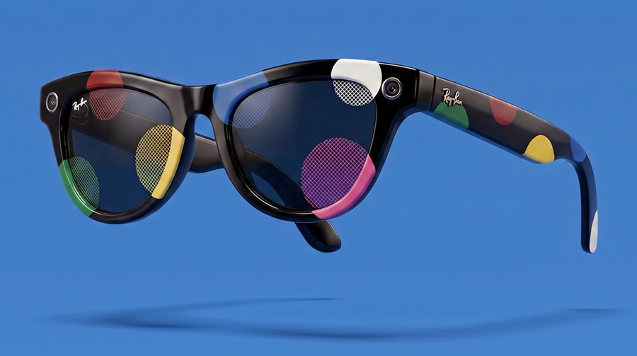 Une vue de profil en studio des lunettes connectées personnalisées Ray-Ban Meta, modèle « Graphic Pop », flottant sur un fond bleu vif uni. La monture noire brillante est ornée de motifs graphiques colorés de style pop-art (pastilles rouges, jaunes, vertes, blanches et roses) qui se superposent sur le cadre et les verres foncés. De petits objectifs de caméra sont visibles sur les coins supérieurs de la monture.
