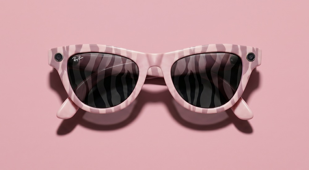 A direct, top-down studio shot of the custom Ray-Ban Meta smart glasses in the "Untamed Glamour" design against a solid pastel pink background. The glasses feature a translucent blush pink frame entirely covered in a bold, muted purple zebra-inspired stripe pattern. The dark sunglass lenses subtly mirror the zebra striping, and a small camera lens is integrated into each upper corner of the frame.