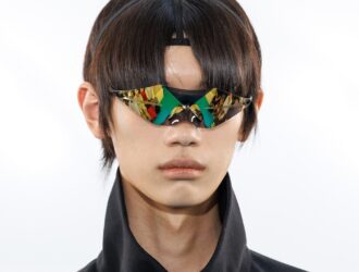 Close-up of Oakley x Kiko Kostadinov FW26 collaboration eyewear featuring a sharp, diamond-scribe silhouette and reflective gold and green tinted lenses.
