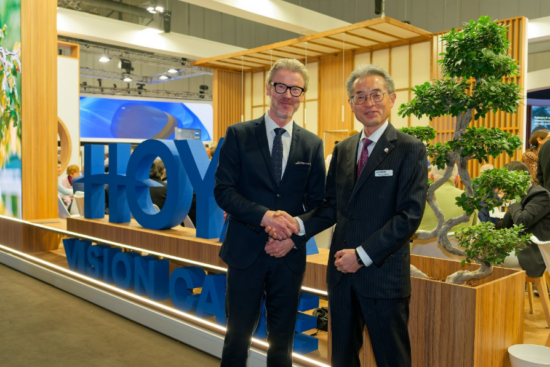 John Goltermann Lassen, CEO of HOYA Vision Care, and Motoki Ozawa, President and CEO of NIDEK, shake hands at the HOYA Vision Care exhibition booth, marking the renewal of their global strategic partnership.