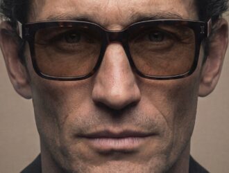 Close-up portrait of a man wearing thick, square, dark tortoiseshell sunglasses with tinted lenses from the NIRVAN JAVAN SHADES OF MILAN collection.