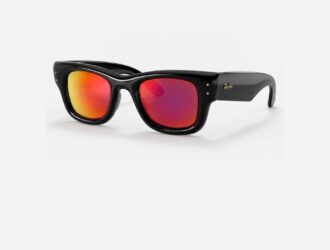 A three-quarter view of Ray-Ban Puffer sunglasses featuring a thick, oversized, glossy black frame with an inflated aesthetic. The lenses are a vibrant, mirrored gradient transitioning from hot pink to bright orange-red. The temples are wide with a gold Ray-Ban logo, and small gold accents are visible on the front chassis