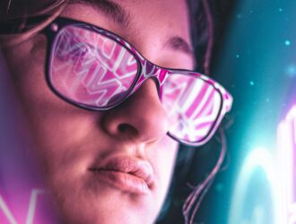 Close-up of a person wearing glasses that reflect vibrant, pink neon text, set against a cyberpunk-style blue and purple background.