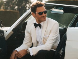 L'icône du tennis Roger Federer portant des lunettes de soleil élégantes Oliver Peoples, vêtu d'un smoking blanc de luxe dans une voiture décapotable de collection pour la campagne été 2026 à Rome.