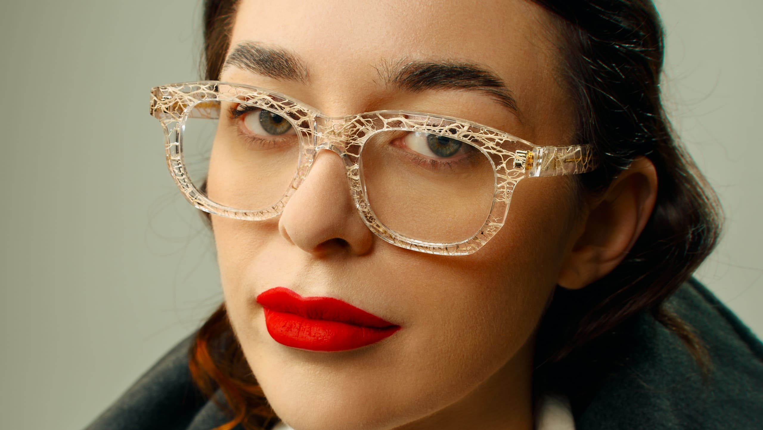 Portrait en gros plan d'une femme portant des lunettes de vue éco-responsables Ferilli Eyewear transparentes avec du rouge à lèvres rouge