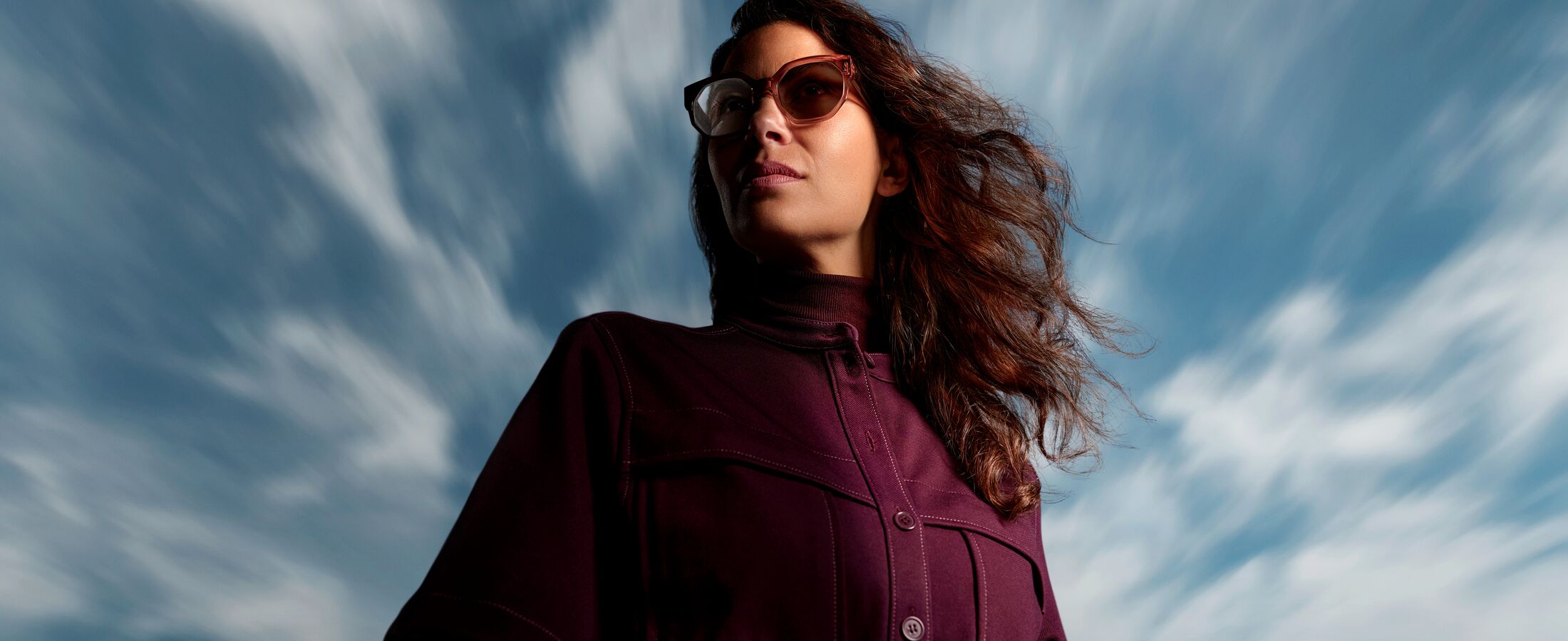 Woman wearing HOYA Sensity 3 light-adaptive sunglasses with Bronze Brown tint outdoors against a dramatic sky