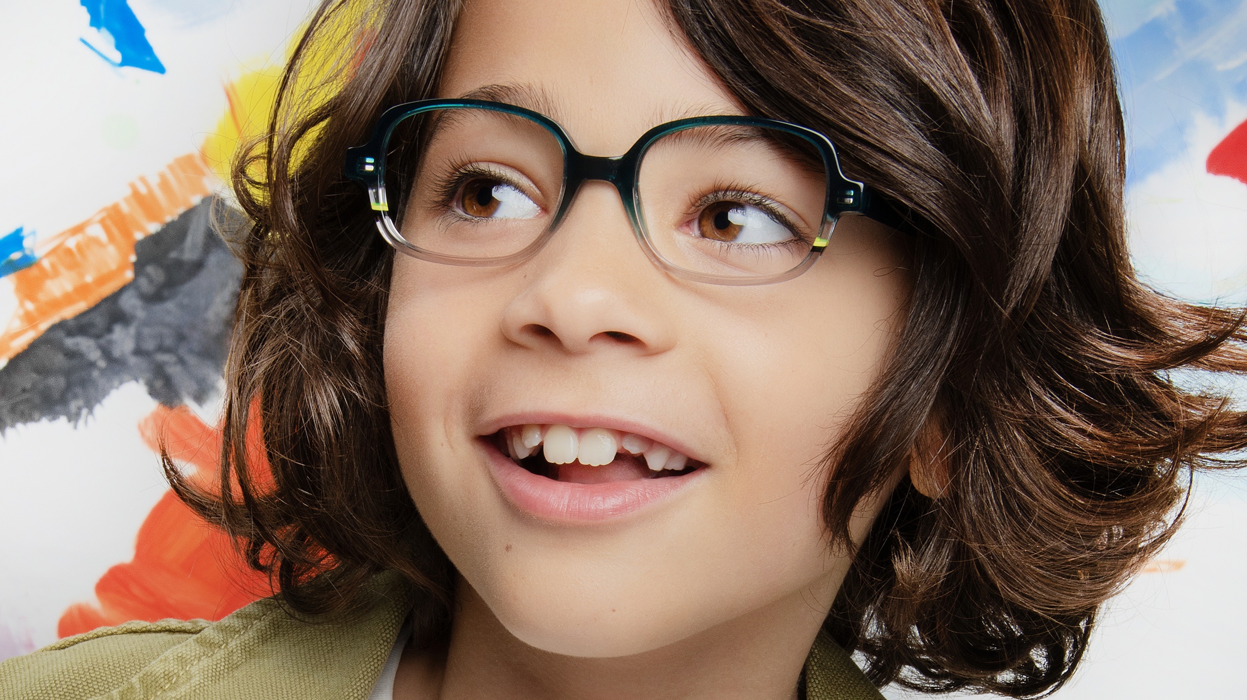 Enfant souriant portant des lunettes J.F. Rey Kids IMAGINE en acétate turquoise, fond coloré et créatif