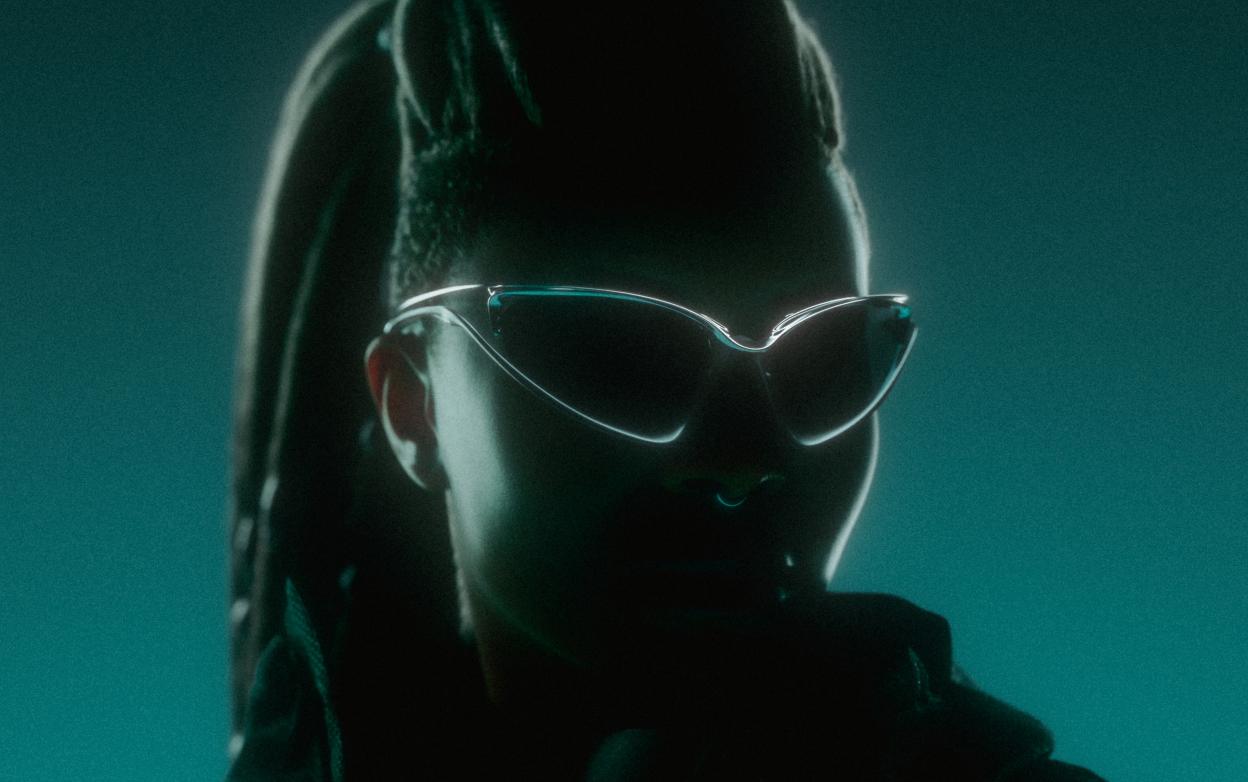 Silhouette portrait of brand hero Maxine Fearlight wearing the Oakley Infiniloop sunglasses against a glowing teal backdrop.