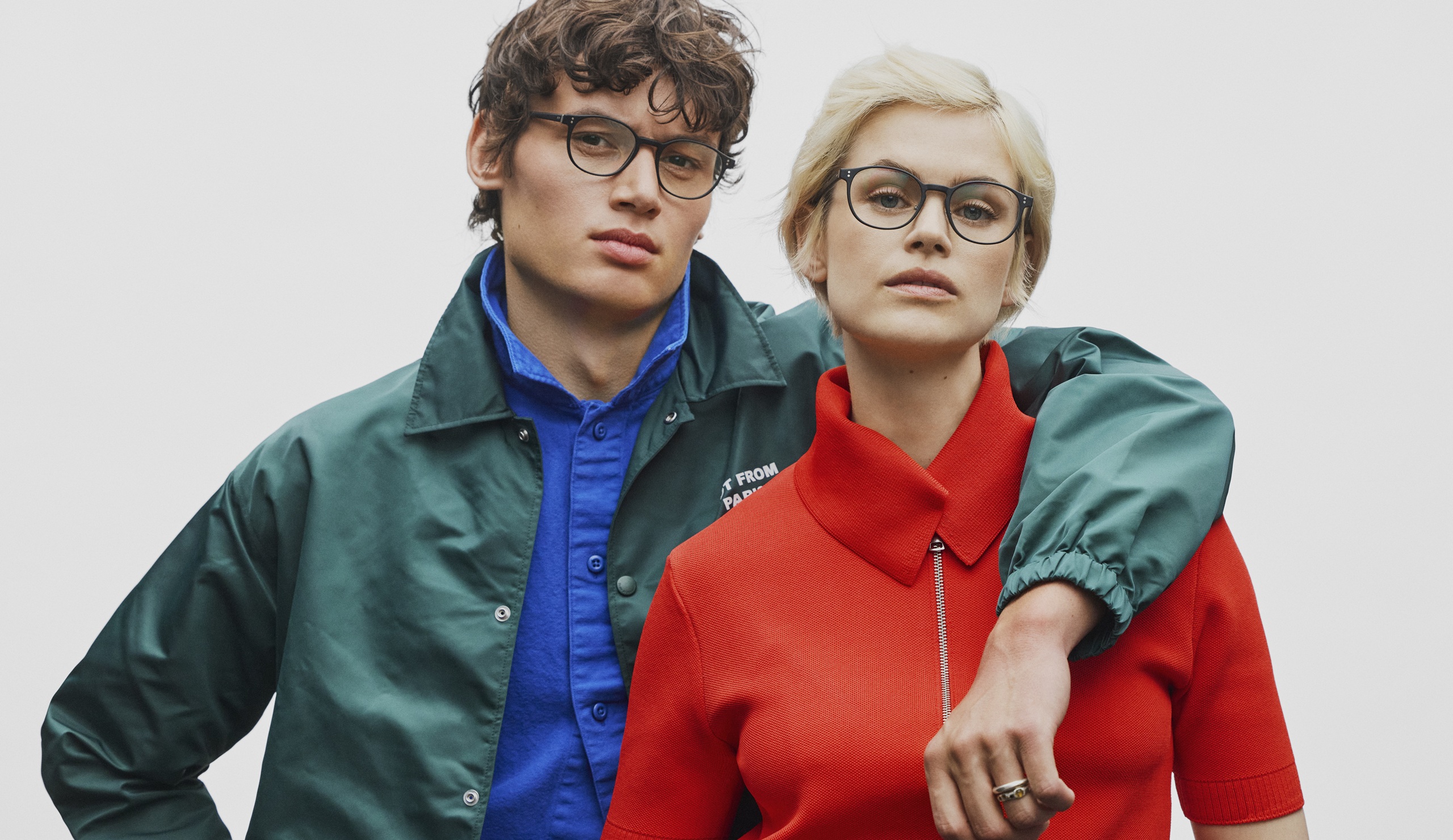 Deux mannequins présentant des montures Prodesign Denmark, l'homme porte une veste verte et la femme un haut rouge, mettant en valeur des styles de lunettes au caractère affirmé.