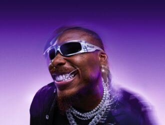 Justin Jefferson souriant avec les lunettes de soleil Oakley Highland en effet verre argenté translucide, verres Prizm Black et détails chromés sur fond violet.