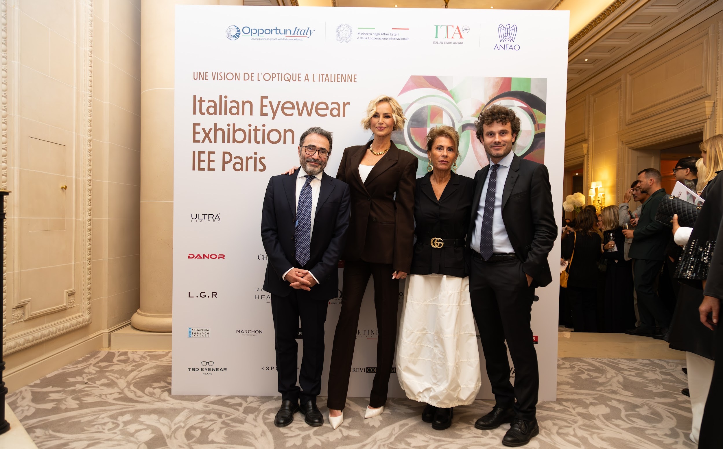 Four people posing at the IEE Paris 2026 Italian Eyewear Exhibition step-and-repeat backdrop, with ANFAO, ITA and Ministero degli Affari Esteri logos and Italian eyewear brand names visible behind them