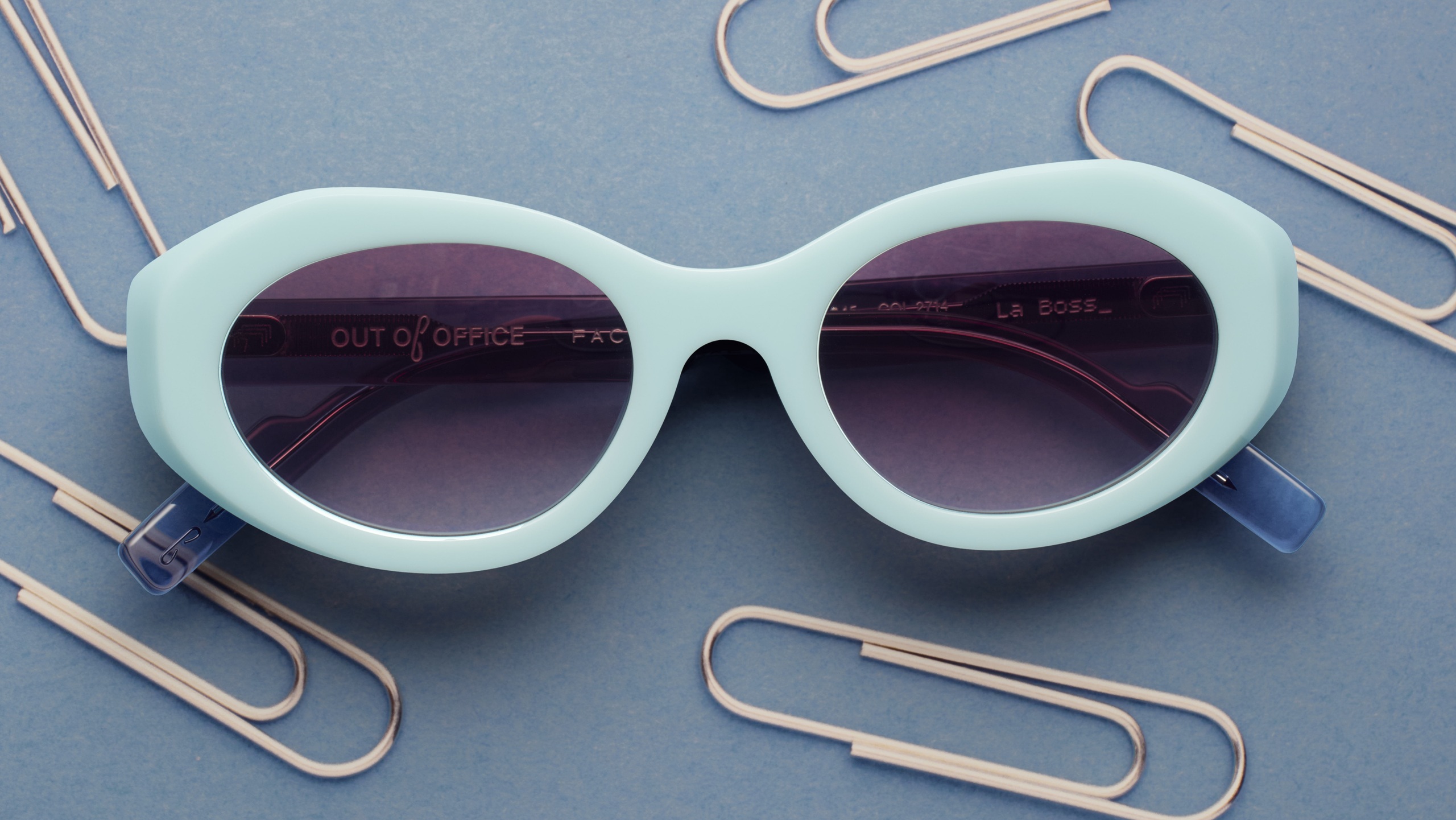 Face à Face Out of Office La Boss light blue oval sunglasses displayed flat lay over paper clips