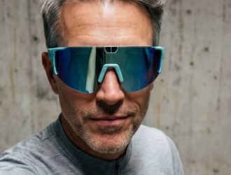 Un homme portant un maillot de cyclisme gris KITS et des lunettes connectées de cyclisme Pangolin 3 à verres réfléchissants bleus.
