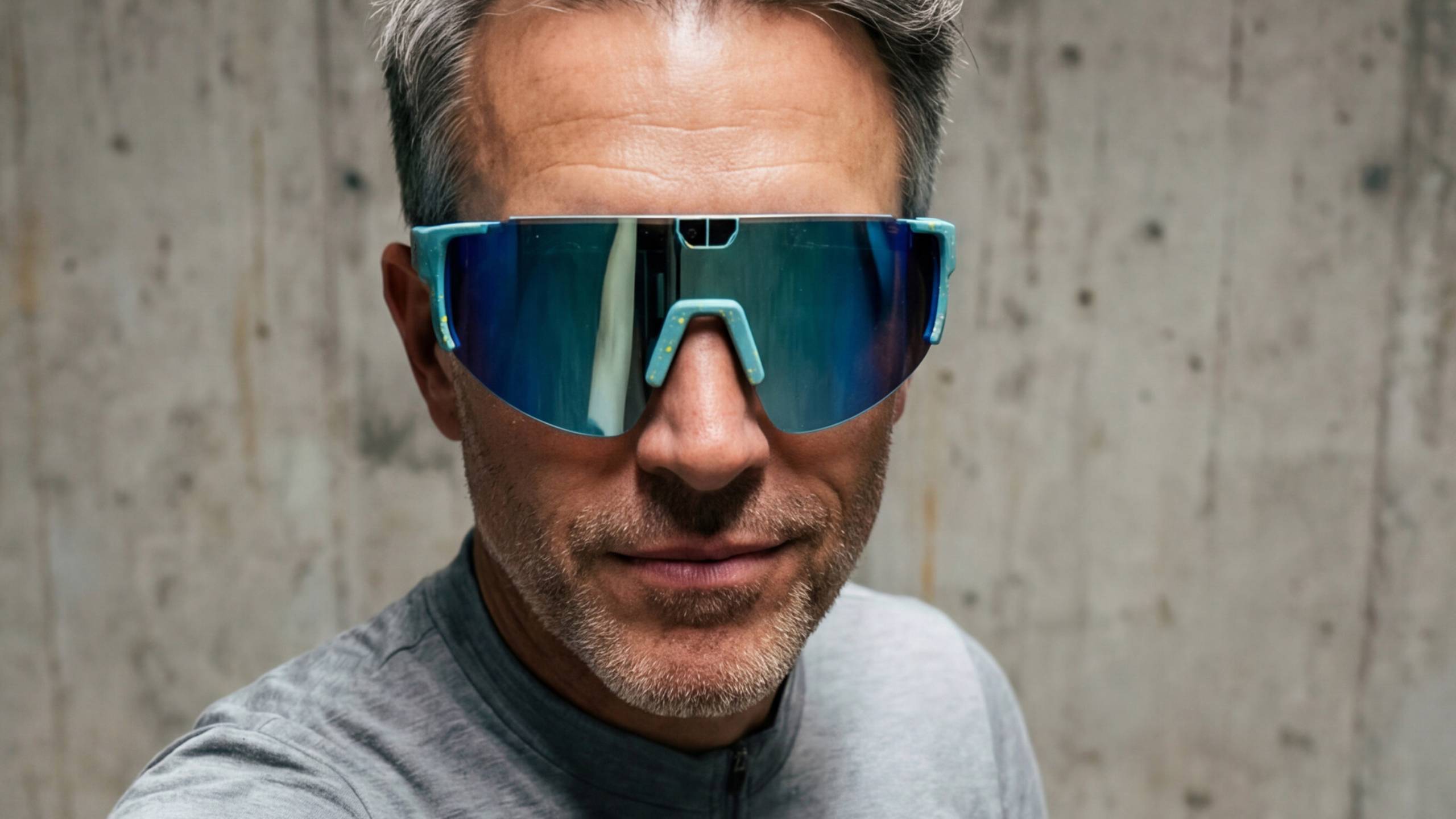 A man wearing KITS grey cycling apparel and Pangolin 3 smart cycling glasses with blue reflective lenses.