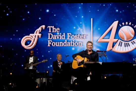 Le musicien Chad Kroeger joue de la guitare acoustique sur scène devant un écran bleu affichant le logo du 40ème anniversaire de la David Foster Foundation.