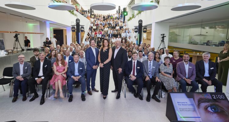 Grand rassemblement de personnes dans le hall moderne du Vision Centre de CooperVision lors de son inauguration, avec l'Ã©quipe et les invitÃ©s installÃ©s dans le grand atrium.