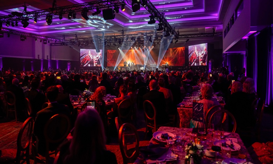 Une vue grand angle d'une salle de banquet bondée éclairée par des lumières d'ambiance violettes pendant une performance lors d'un gala.