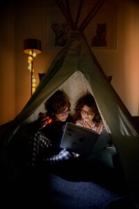 Deux jeunes enfants portant des lunettes de vue lisent ensemble dans une tente d'intérieur confortable, illustrant la performance de la vision de près avec les verres de lunettes de contrôle de la myopie DOT.