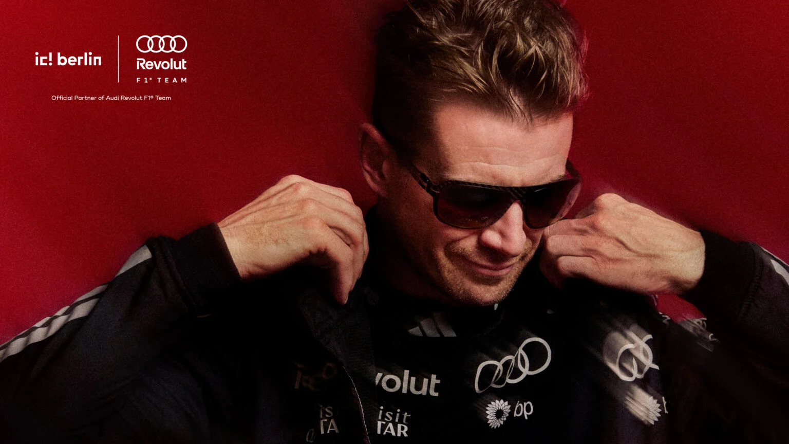 Close-up portrait of Nico Hülkenberg adjusting his team jacket while wearing dark ic! berlin sunglasses with a motion-blur effect.