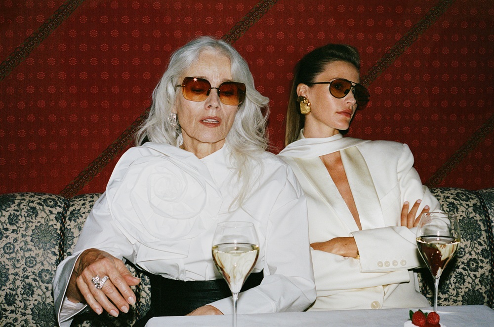 Two elegant women wearing luxury LINDA FARROW SS27 sunglasses seated at a high-end hotel bar with champagne glasses.