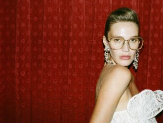 Une femme portant des montures optiques à verres transparents surdimensionnées LINDA FARROW SS27 contre un fond de rideau en velours rouge riche.