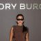 Maia Reficco poses in front of the Tory Burch step-and-repeat wall wearing sleek black sunglasses and a brown striped one-shoulder top, her dark hair pulled into a low ponytail.