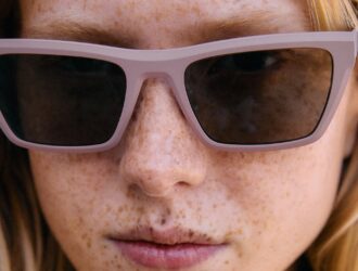 Gros plan d'un visage avec des taches de rousseur portant les lunettes de soleil Ørgreen Sheet Titanium SUN, avec une monture lavande mate et des verres fumés.