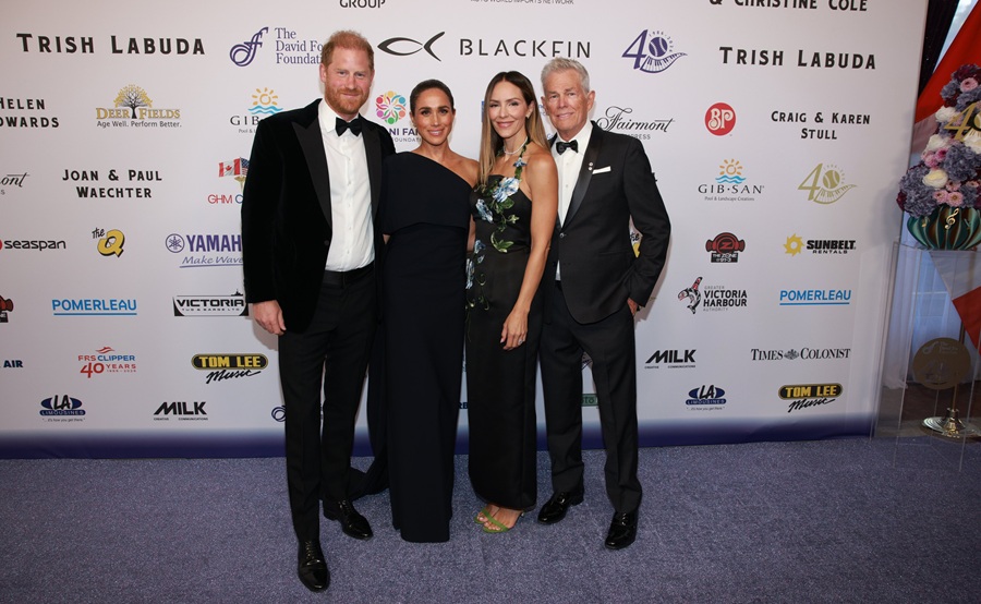 Prince Harry, Meghan Markle, Katharine McPhee, and David Foster posed together on a red carpet in front of a sponsor backdrop.