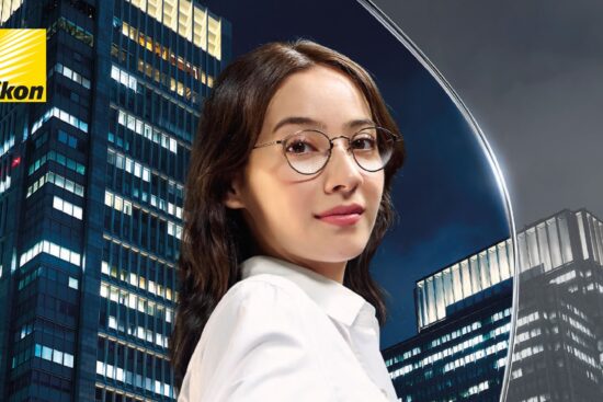 Affiche publicitaire Nikon pour les lentilles Z Series Simple Vision, montrant une femme portant des lunettes de vue tendant la main devant un arrière-plan de gratte-ciel illuminé, avec le titre « VIVEZ LA VIE EN HAUTE DÉFINITION : UNE NOUVELLE ÈRE DE LENTILLES SIMPLE VISION ».