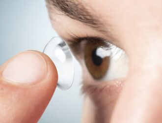 Gros plan sur une personne qui utilise le bout de son doigt pour insérer une lentille cornéenne transparente dans son œil marron.